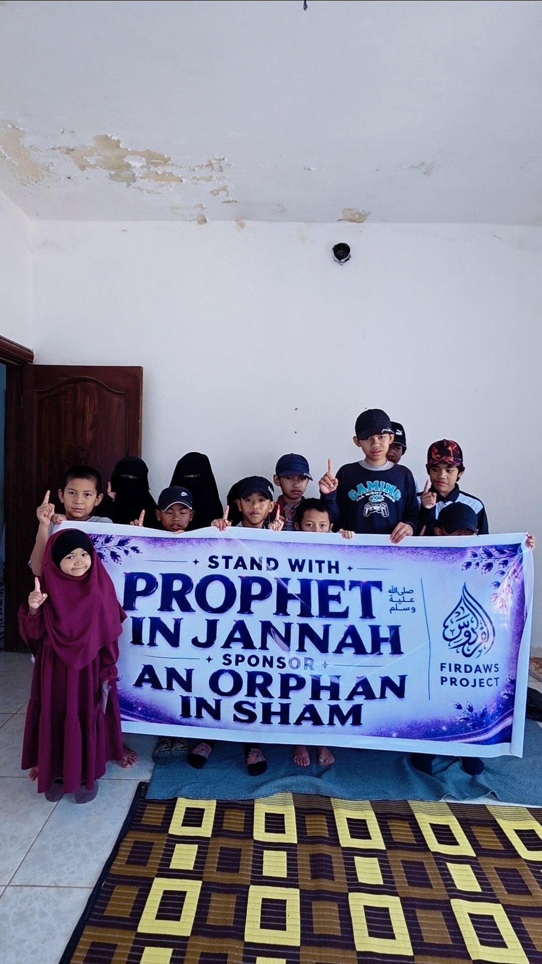 Orphans holding a Firdaws Project sponsor an orphan banner in Sham